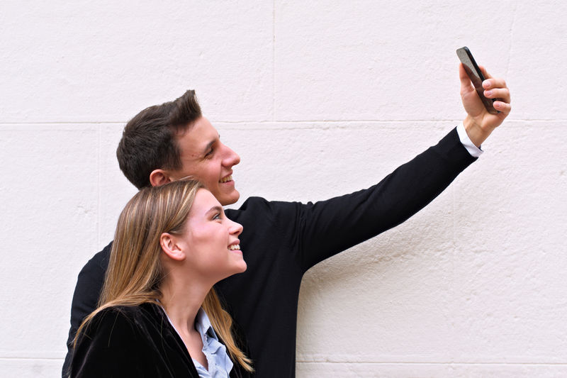 Portrait of smiling young woman using mobile phone against wall