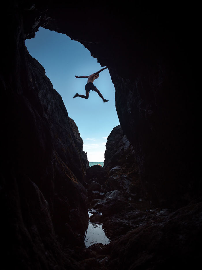 Low angle view of man jumping over rock formation against sky