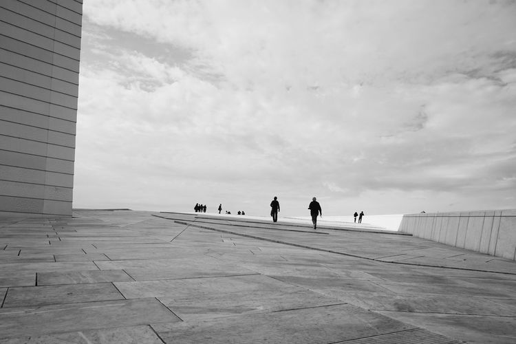 People at oslo opera house against cloudy sky