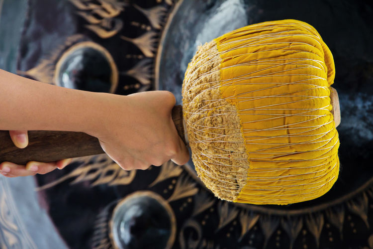 Midsection of woman banging gong with yellow mallet