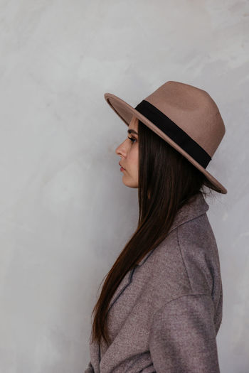 Woman in beige cashmere coat and beige hat against the background of a white wall turned sideways