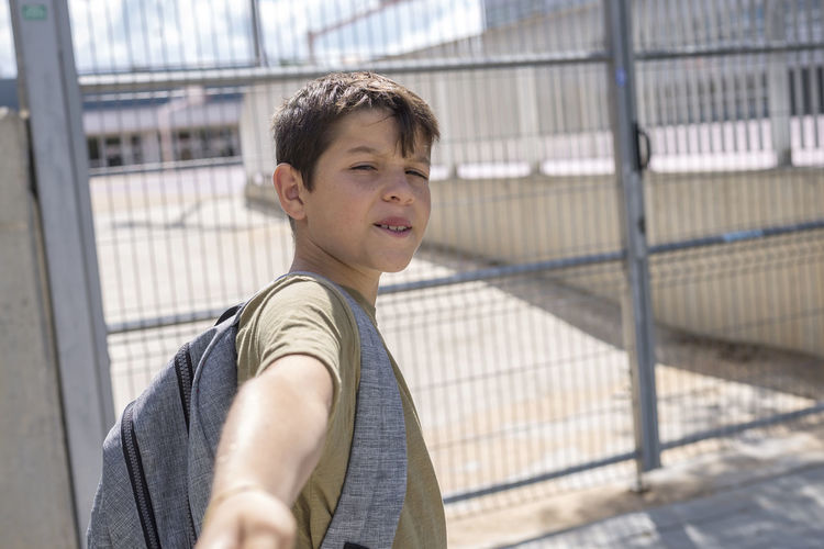 Portrait of smiling boy standing by fence in schoolyard