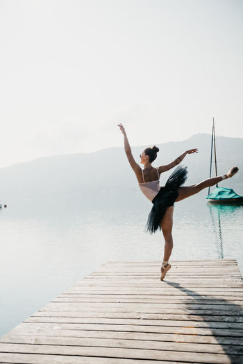 Ballet dancer dancing on pier over lake against mountains