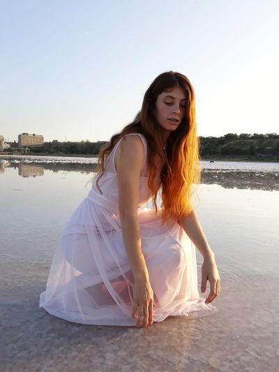 Beautiful young woman against water against sky