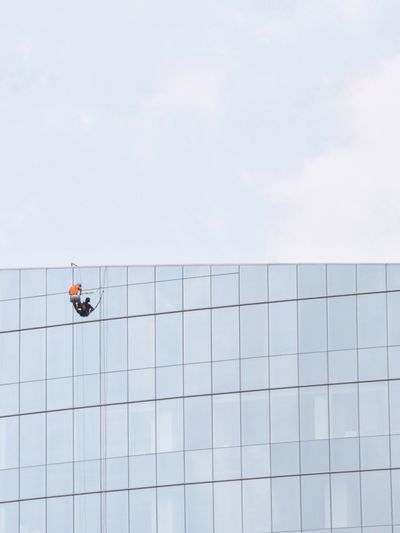 Low angle view of worker washing window on building against clear sky