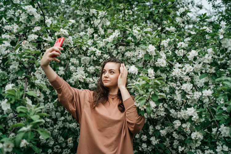 Girl in blooming apple tree using smartphone video call outdoor nature