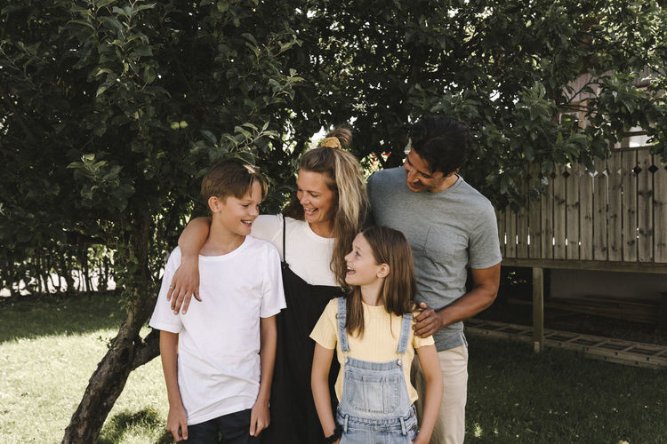 Smiling parents with children against tree in front yard