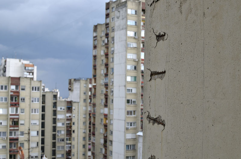 Damaged concrete wall with visible iron construction of a skyscraper and buildings