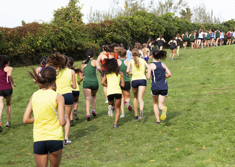 Rear view of high school girls running uphill on grass during a cross country race at bowdoin park