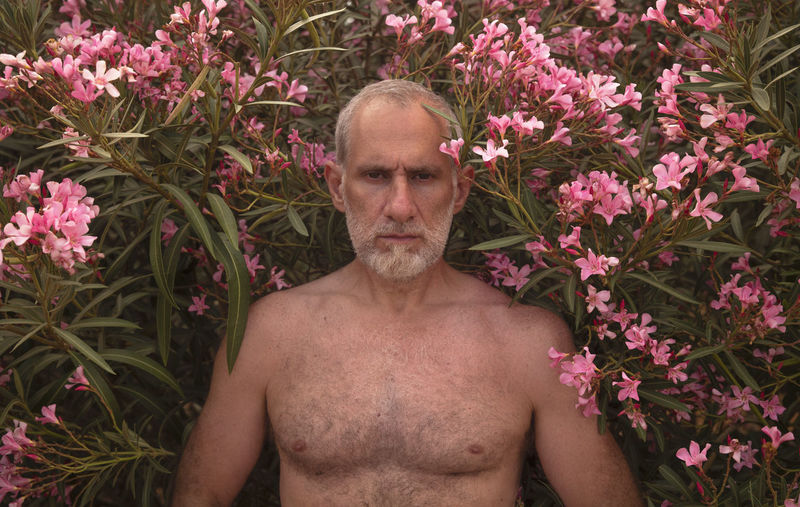 PORTRAIT OF SHIRTLESS MAN STANDING ON FLOWERING PLANTS