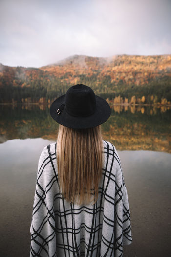 Hipster caucasian woman in a poncho and hat in the autumn time in colorful forest near the lake