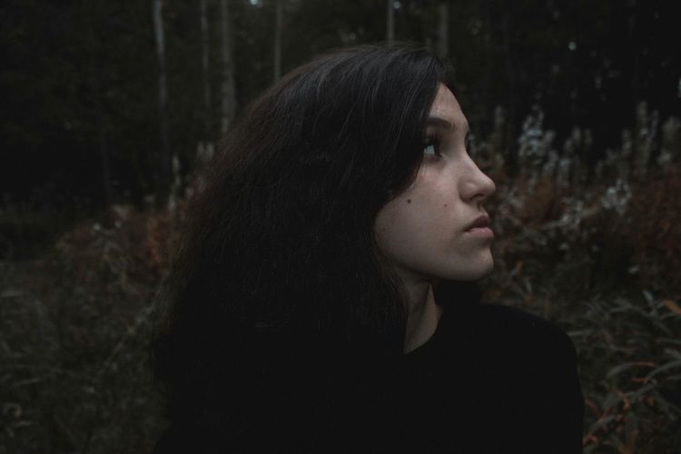 Close-up portrait of a young woman looking away in forest