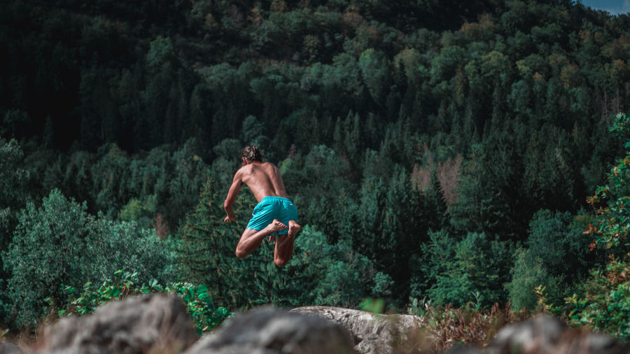 Full length of shirtless man jumping in forest