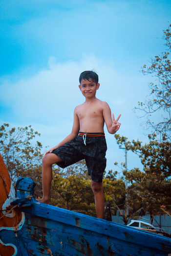 Portrait of shirtless boy standing against sky
