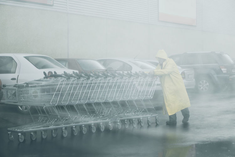 Senior man pushing shopping cart while walking on street during rainfall