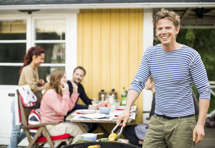Portrait of happy man barbecuing with friends at dining table in background