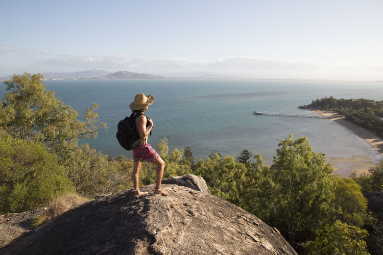 Backpacker with hat and swimsuit, on top of rocky hill during sunset