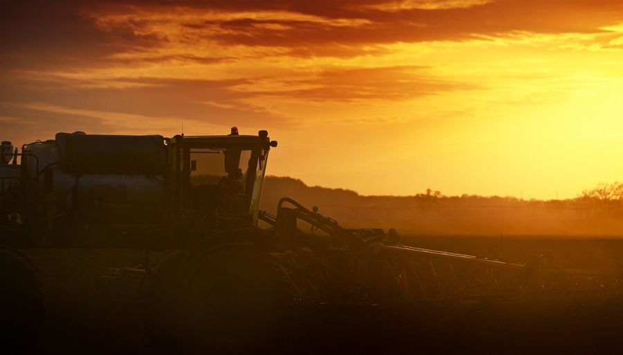 Agricultural machinery on field against sky during sunset