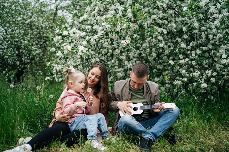 Family mom mom baby daughter in the garden blooming apple trees, father playing the ukulele