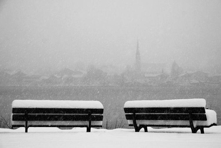 Snow covered benches against sky during snowfall