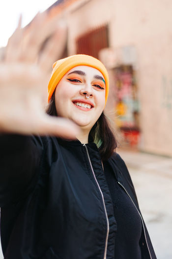Positive female with makeup showing stop gesture and looking at camera while standing on street with buildings on blurred background