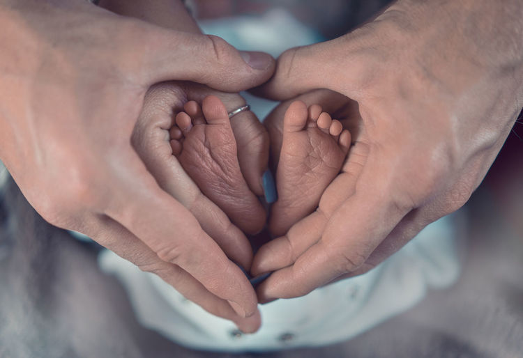 Cropped hands of parents making heart shape with baby feet