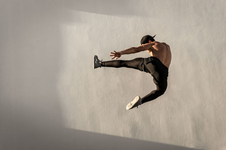 Full length of shirtless man jumping against wall