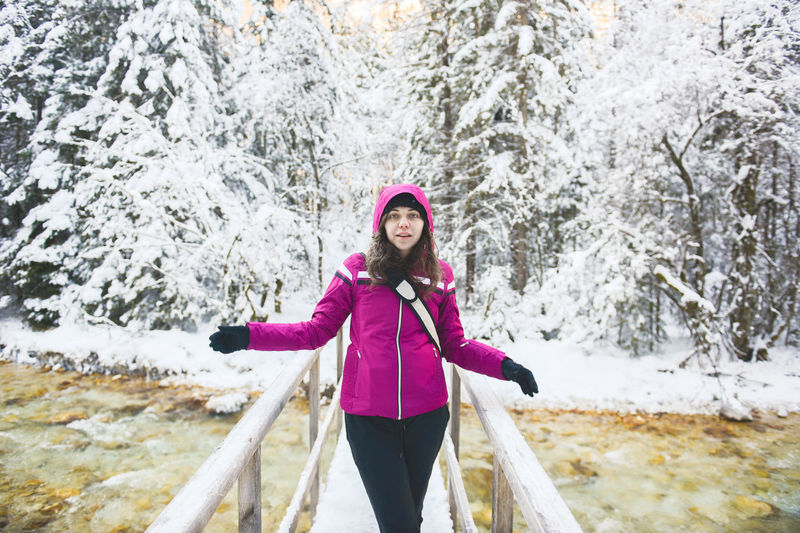 Woman standing on footbridge over river against trees during winter