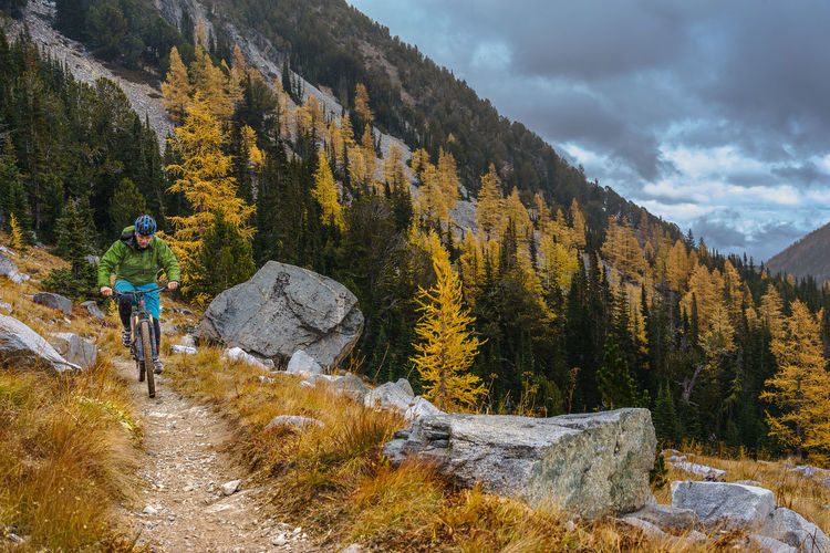 Hiker riding mountain bike on trail against cloudy sky during autumn