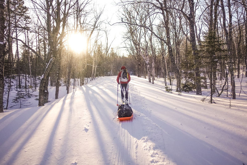 Skier pulling pulk sled on a trail at sunrise