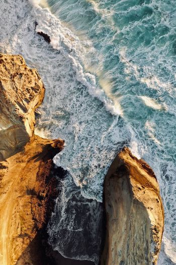 High angle view of waves splashing on rocks at beach during sunset