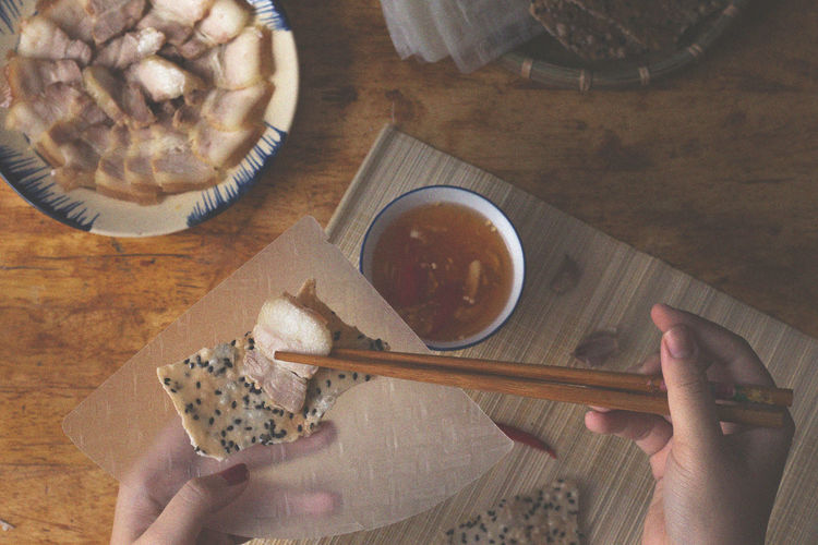 High angle view of hand holding meat with chopsticks over cracker