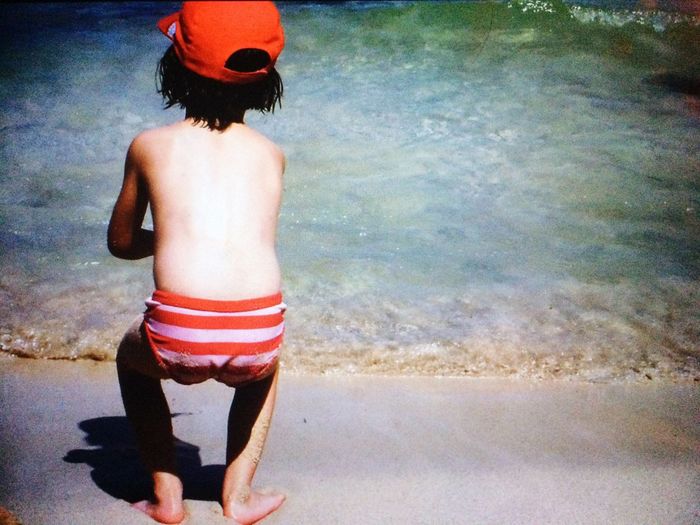 Rear view of shirtless boy standing in water
