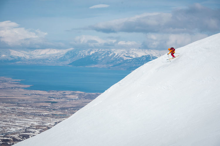 A man jumps off a ski jump on a mountain in iceland with water behind