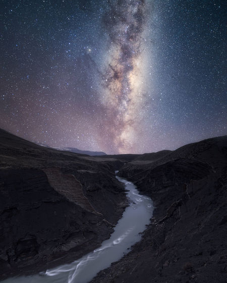 Scenic view of stream amidst mountains against star field at night