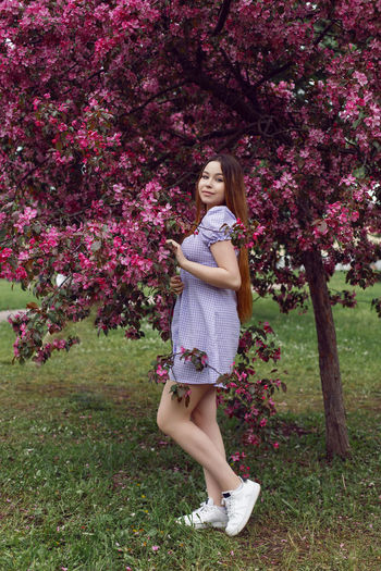 Portrait young beautiful girl teenager in a purple dress and  stands blooming pink apple tree