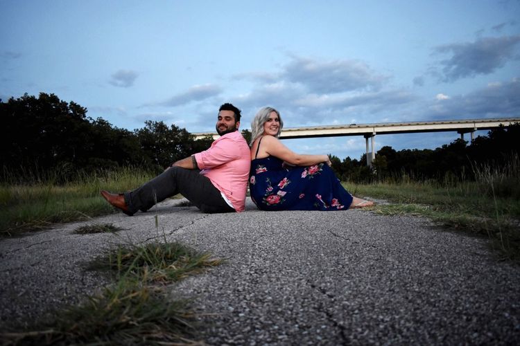 Young couple sitting on road against sky