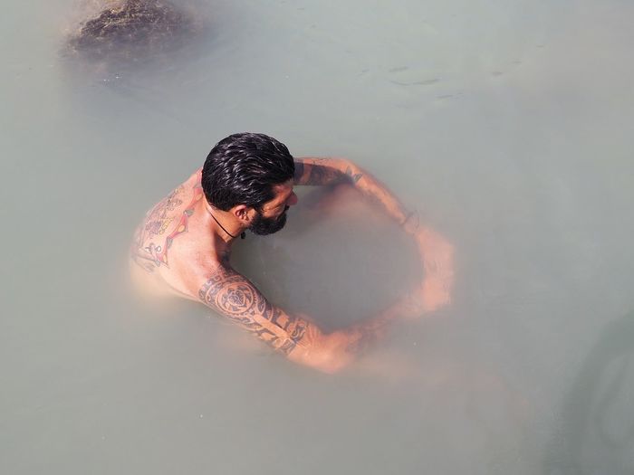 High angle view of shirtless tattooed man sitting in sea