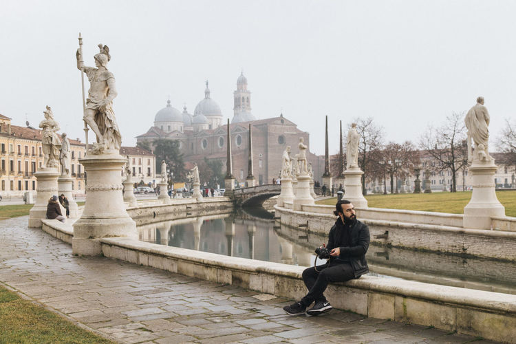 Statue of man sitting in city against sky