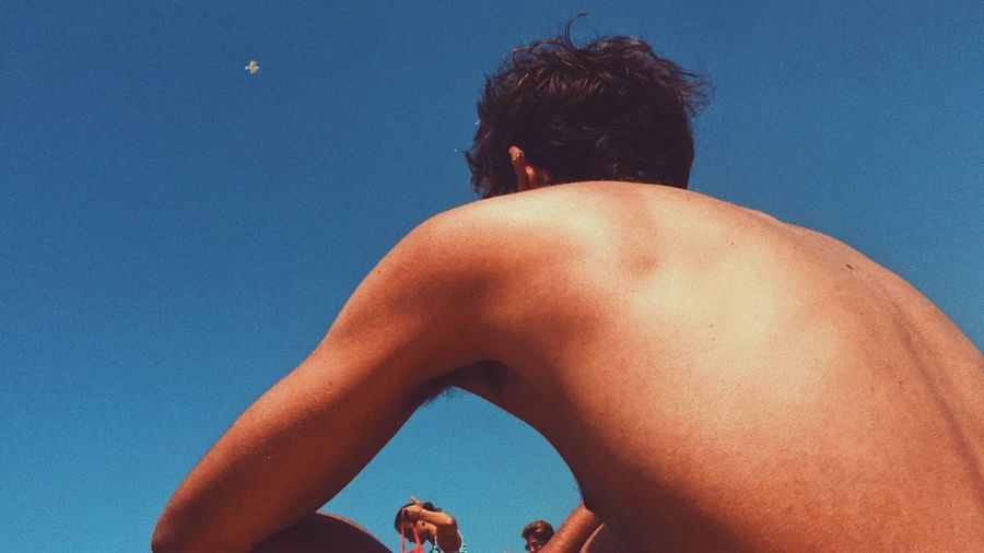 Rear view of shirtless man against blue sky