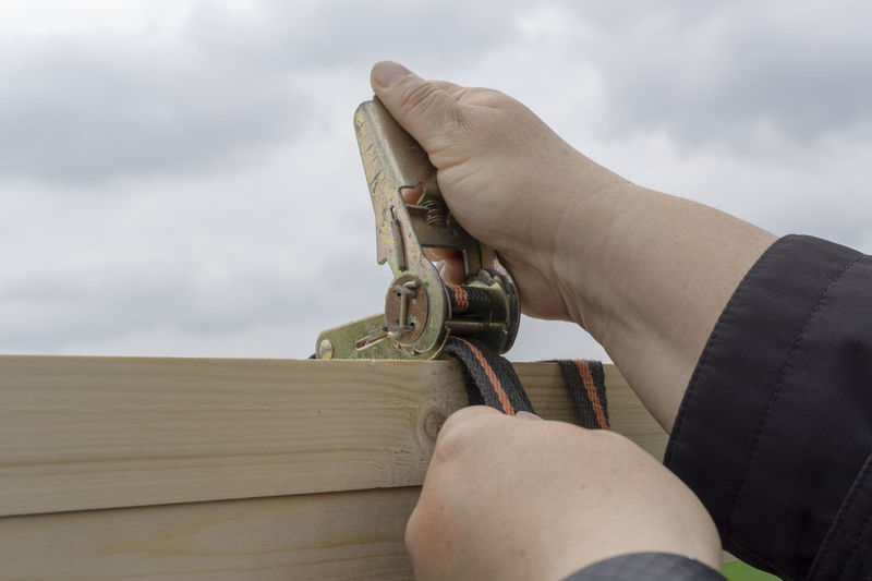 Close-up of hand holding equipment on wood against sky