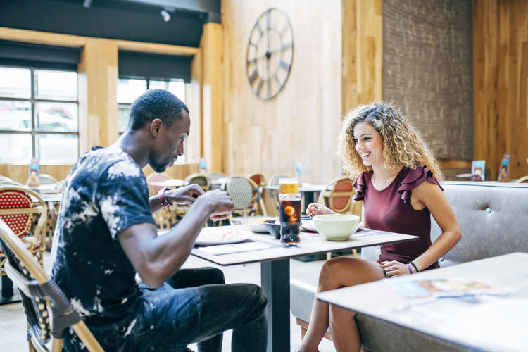 Blonde woman and african man enjoy eating in restaurant.
