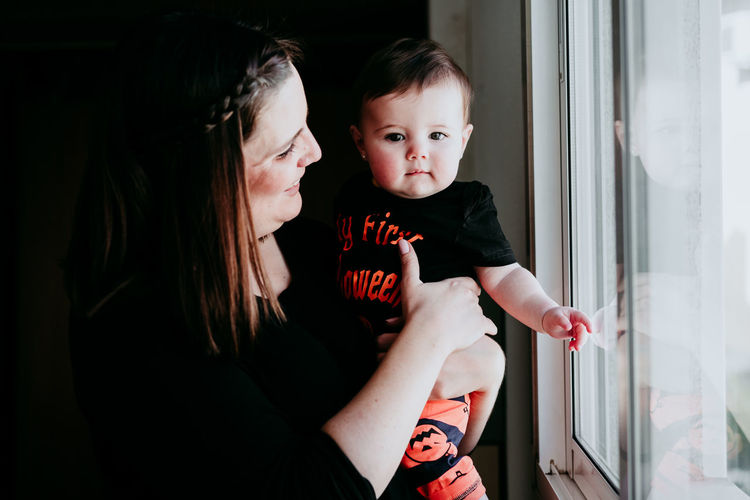 Portrait of cute girl with mother standing by window at home