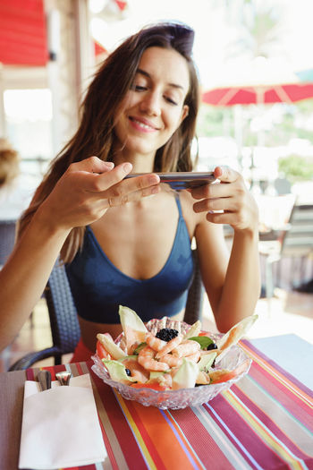 Young woman taking photograph of food at table in restaurant