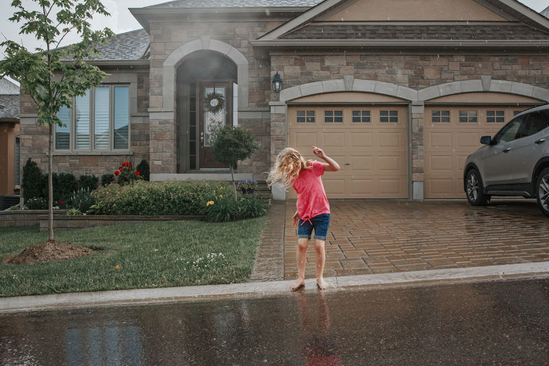Girl splashing under rain in front of house. child having fun during rain shower storm