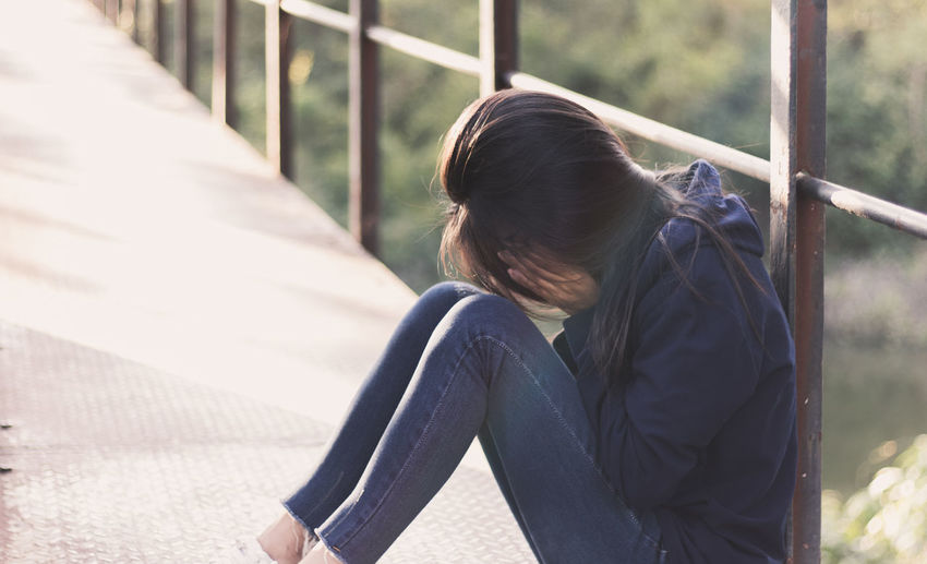 Side view of depressed woman covering face while sitting on footbridge