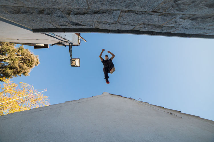 Low angle view of man jumping against clear sky