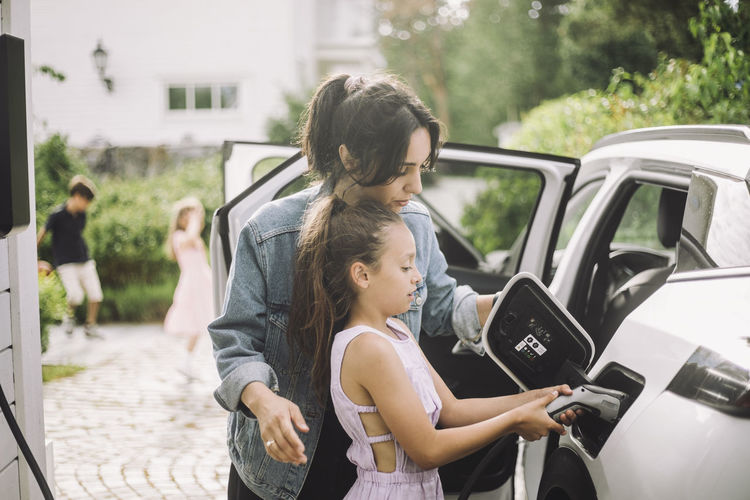 Mother teaching daughter to plug charger in electric car