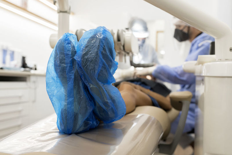 Anonymous patient in blue plastic shoe covers lying on chair and getting treatment in dental clinic