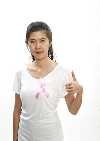 Portrait of smiling woman showing thumbs up while wearing pink ribbon on top against white background